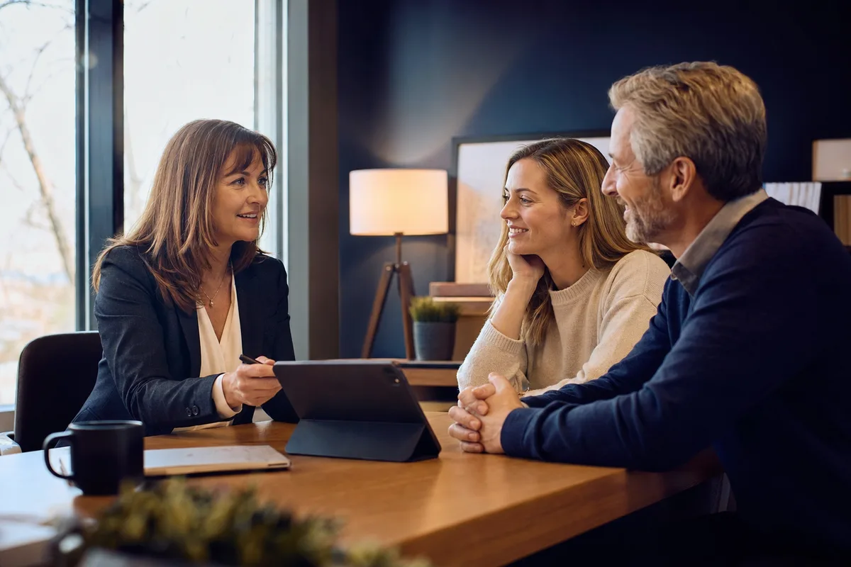 A financial advisor reviewing a financial plan on a tablet with a client couple across her desk